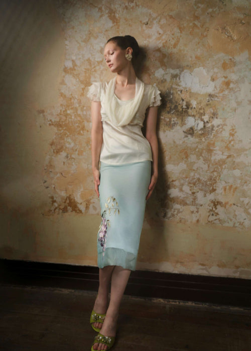 Model in a mint green silk organza midi skirt with wisteria embroidery at the hem, styled with an ivory top, front view